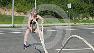 Athletic female working out using battle ropes. Crossfit