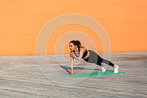 Athletic fit pretty girl in sportswear, black pants and top, practicing yoga, standing in Phalakasana higher plank pose