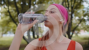Athletic fit sport jogger young woman drinking water from bottle after training exercising in park
