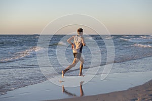 Athletic fit and strong runner man training on Summer sunset beach in sea shore running and fitness workout in sport and healthy l