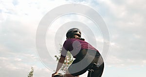 Athletic fit woman cyclist is pedaling on aero bike in park at sunset. Sportive female athlete is cycling on bicycle, rear view. P