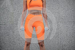 Athletic fitness woman with dumbbells. Sporty girl prepares for workout arm muscle, sabs, abdominals with dumbbells outdoors