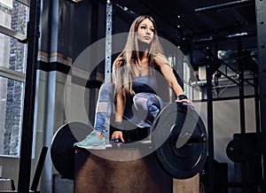 Athletic fitness woman wearing sportswear posing on a stand with a barbell in a gym