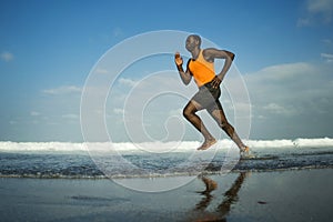 Athletic full body portrait of young attractive and fit black African American man running on the beach doing Summer fitness