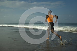 Athletic full body portrait of young attractive and fit black afro American man running on the beach doing Summer fitness jogging