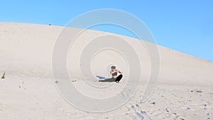 Athletic girl in black top and leggings performs stretching in twine pose, sits on the gymnastic twine on a deserted