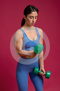 Athletic girl doing dumbbell bicep curl on maroon background