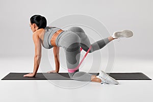 Athletic girl doing exercise for glutes with resistance band on gray background. Fitness woman working out