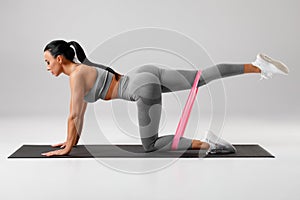 Athletic girl doing kickback exercise for glutes with resistance band. Fitness woman working out donkey kicks