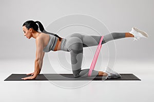 Athletic girl doing kickback exercise for glutes with resistance band. Fitness woman working out donkey kicks photo