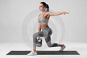 Athletic girl doing lunges exercises with kettlebell, leg muscle training. Fitness woman doing front forward one leg step lunge