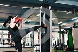 Athletic girl makes a kick on the punching bag. woman in boxing gloves trains martial arts.