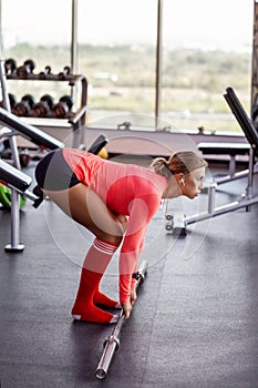 Athletic girl performs exercises with a barbell. A young woman in sportswear does the slopes. Fitness, workout