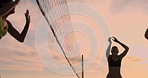 Athletic girl playing beach volleyball jumps in the air and strikes the ball over the net on a beautiful summer evening