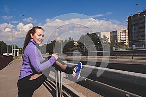 athletic girl stands with her foot on the railing of the bridge, workout urban sport concept