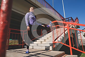 Athletic girl stands with her foot on the railing of the stairs, workout urban sport concept
