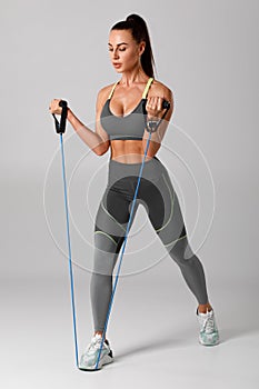 Athletic girl working out with resistance band on gray background. Fitness woman exercises with expander