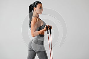 Athletic girl working out with resistance band on gray background. Fitness woman exercises with expander