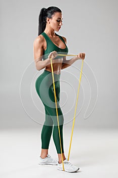Athletic girl workout with resistance band on gray background. Fitness woman doing exercise for biceps