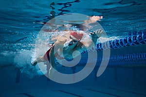 Athletic grace and strength. Young man in cap and goggles, swimmer in motion underwater training in swimming pool