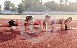 Athletic group of women training on a sunny day doing planking exercise in the stadium. photo