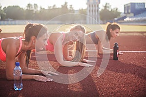 Athletic group of women training on a sunny day doing planking exercise in the stadium. photo