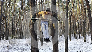 Athletic guy doing push ups on horizontal bar at winter forest. Hardy sportsman exercising outdoor. Strong and muscular