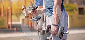 Athletic guy and girl doing exercises with dumbbells at the sports field