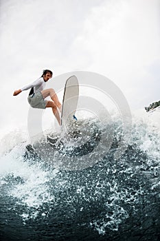 Athletic guy having fun and jumps at wave on wakesurf board in the summer day. photo