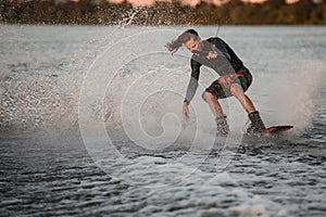 Athletic guy holds rope and energetically riding wakeboard on splashing river water.