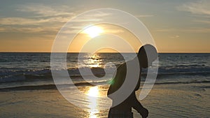 Athletic guy jogging along ocean shore during sunrise. Young sporty man running on the sea beach at sunset. Male