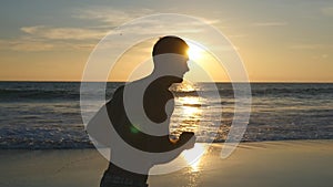 Athletic guy jogging along ocean shore during sunrise. Young sporty man running on the sea beach at sunset. Male