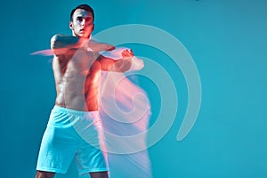 Athletic guy with naked torso raised arms performing dance on blue studio background. Copy space. Long exposure