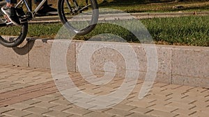 An athletic guy rides a BMX stunt bike in the Park, he jumps on the curb.