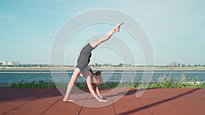 Athletic Gymnast Woman is training on Lake Background. Beautiful Girl Is Exercising Outdoors. Stretching Exercises and Flexibility