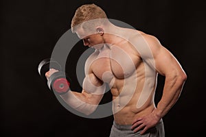 Athletic handsome man fitness-model is working out with dumbbell and showing his perfect body. isolated on black