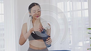 Athletic Healthy Asian young woman in sportswear drinking water after workout excercise at home.Young sporty female take a break