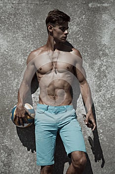 Athletic hot guy with a ball in his hand is posing outdoors