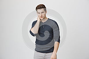 Athletic and hot male model in casual clothes looks at camera while holding his neck with one hand, isolated over white