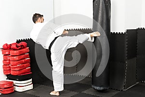 Athletic karate fighter giving a forceful foot kick to a heavy b