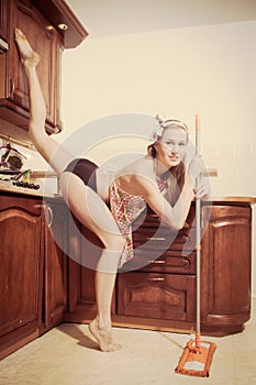 Athletic leg split flexible smiling young blond woman pinup girl sweeping the floor in the kitchen & looking at camera