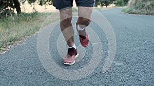 Athletic legs of athletic strong mature sportman running outside road through field.