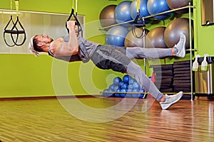 Athletic male exercising with trx straps in a gym club.