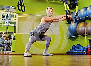 Athletic male exercising with trx straps in a gym club.
