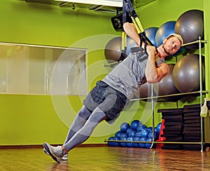 Athletic male exercising with trx straps in a gym club.