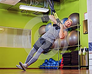 Athletic male exercising with trx straps in a gym club.