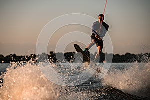 athletic male wakeboarder jumps with wakeboard over splashing river. Summertime watersports activity