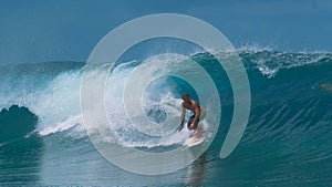 Athletic man on active summer vacation in Tahiti surfs a big emerald tube wave.