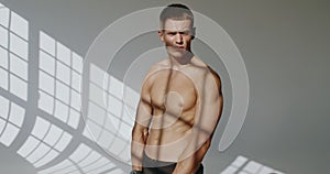 Athletic man bodybuilder with shirtless torso posing on camera in studio