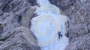 Athletic man with crampons and ice axes climbs up the gorgeous frozen waterfall.